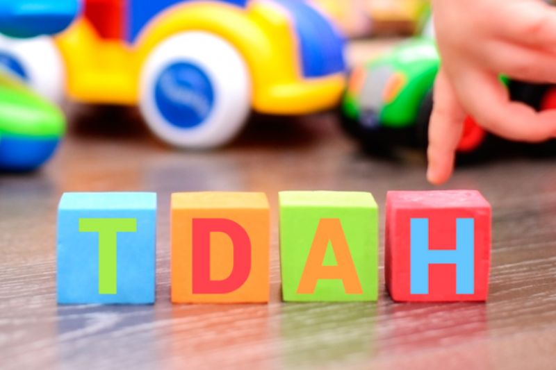Bloques de colores con las letras "TDAH" sobre una mesa, con un fondo de juguetes infantiles.